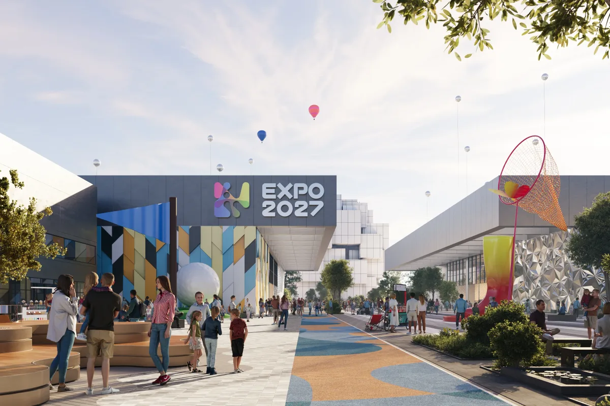 Render of visitors walking along a colourfully paved promenade on the Expo 2027 Belgrade site, past a pavilion with an EXPO 2027 sign and a tall red hoop sculpture