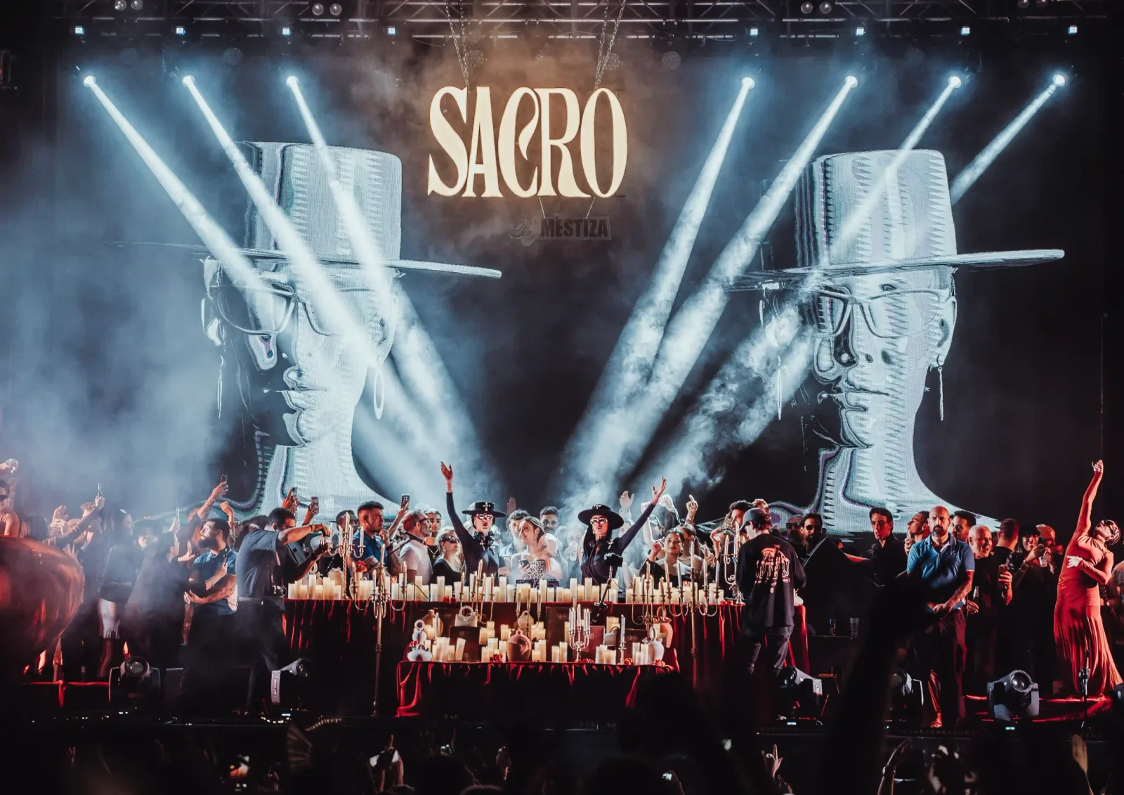 Mestiza on stage at a Sacro night, with a crowd in front of a lit stage and the SACRO logo