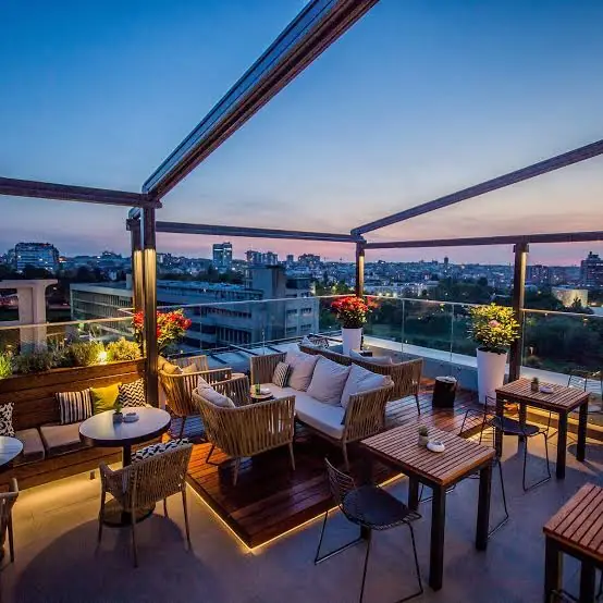 Rooftop lounge terrace in Belgrade at dusk with sofas, cushions, flower planters and a view over the city