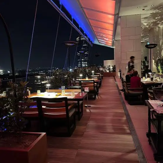 Rooftop terrace in Belgrade at night with blue accent lighting, wooden tables and a view over the city lights