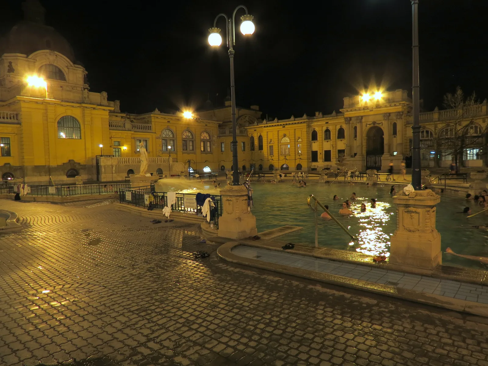 Bassin extérieur des thermes Széchenyi de nuit, façades jaunes éclairées par des lampadaires